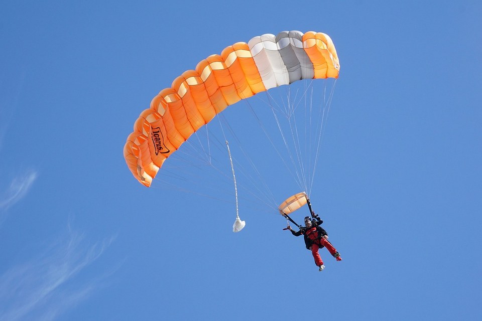 Ein Fallschirmspringer mit orangefarbenem Lenkschirm vor einem klaren, blauen Himmel