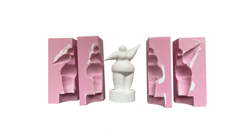 Weiße Nana-Figur zwischen vier geöffneten rosa Silikonformen zur Herstellung der Skulptur.