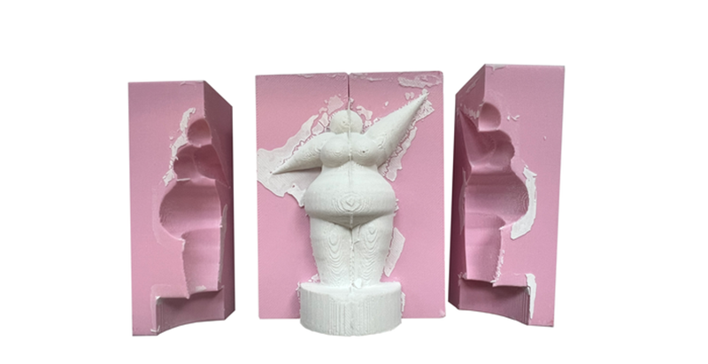 Weiße Nana-Figur in geöffneter rosa Silikonform, daneben zwei weitere Formteile zur Herstellung der Skulptur.