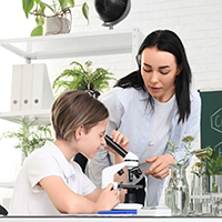 Eine Lehrerin hilft einer jungen Schülerin bei der Arbeit mit dem Mikroskop