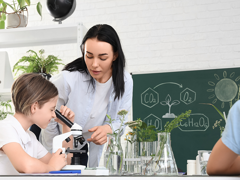 Eine Lehrerin hilft einer jungen Schülerin bei der Arbeit mit dem Mikroskop. Starterbild für den Bereich Biologie