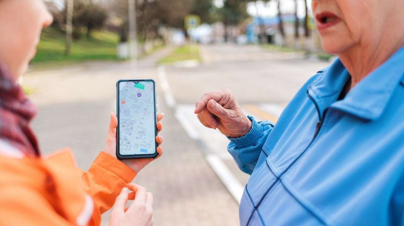Zu sehen ist eine Person, die einer anderen Person einen Stadtplan auf einem Smartphone zeigt.