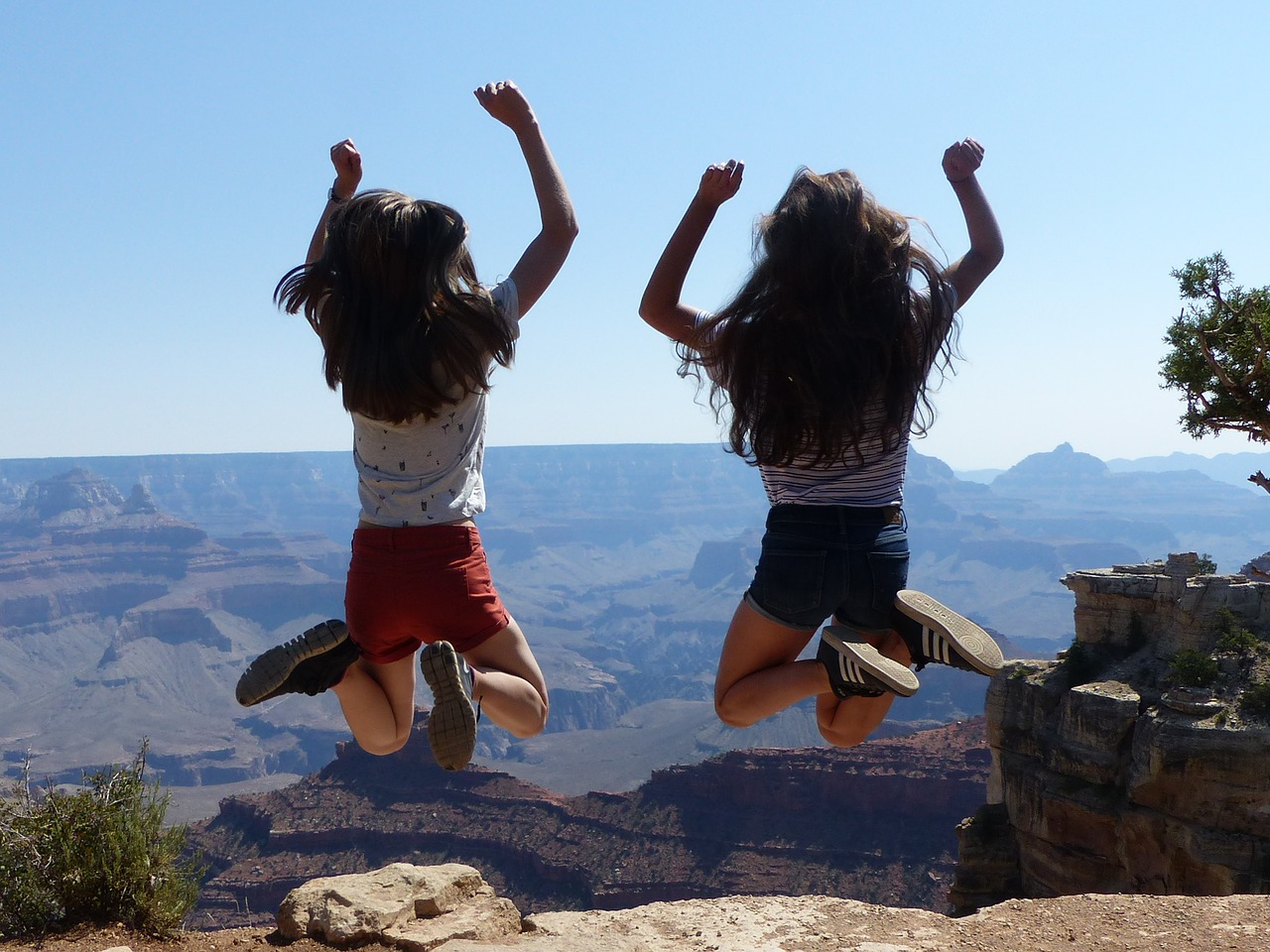 Zwei Teenagerinnen springen vor dem Hintergrund des Grand Canyon in die Luft